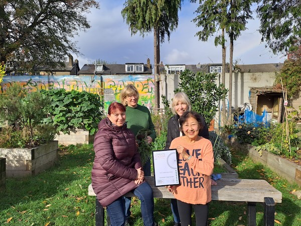 alt="Harlesden Town Garden members show off the 2025 RHS Gold Award for Best Small Garden."